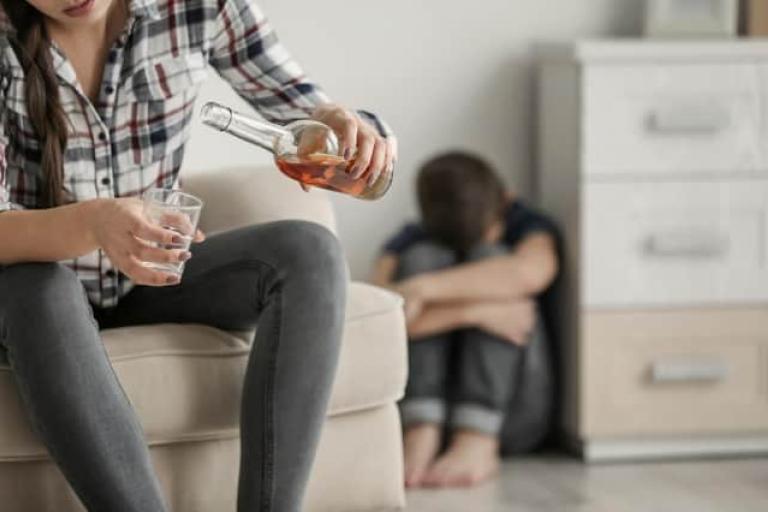 child cowering in corner while parent pours a drink
